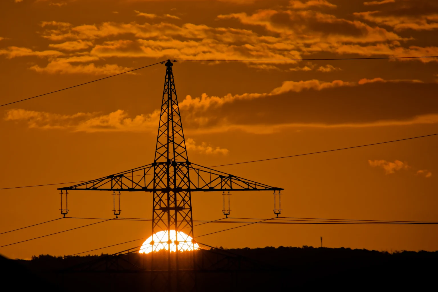 Sonnenaufgang hinter Wolken und einem Strommast.