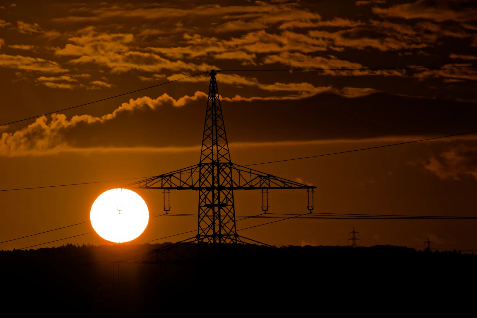Sonnenaufgang hinter Wolken und einem Strommast.