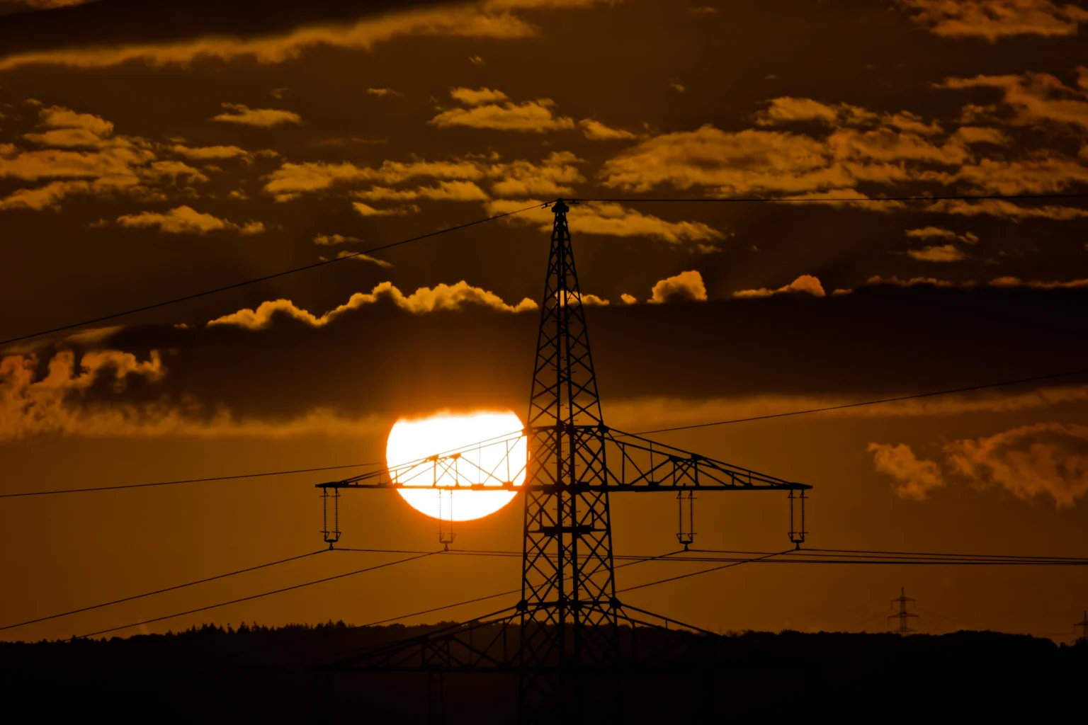 Sonnenaufgang hinter Wolken und einem Strommast.