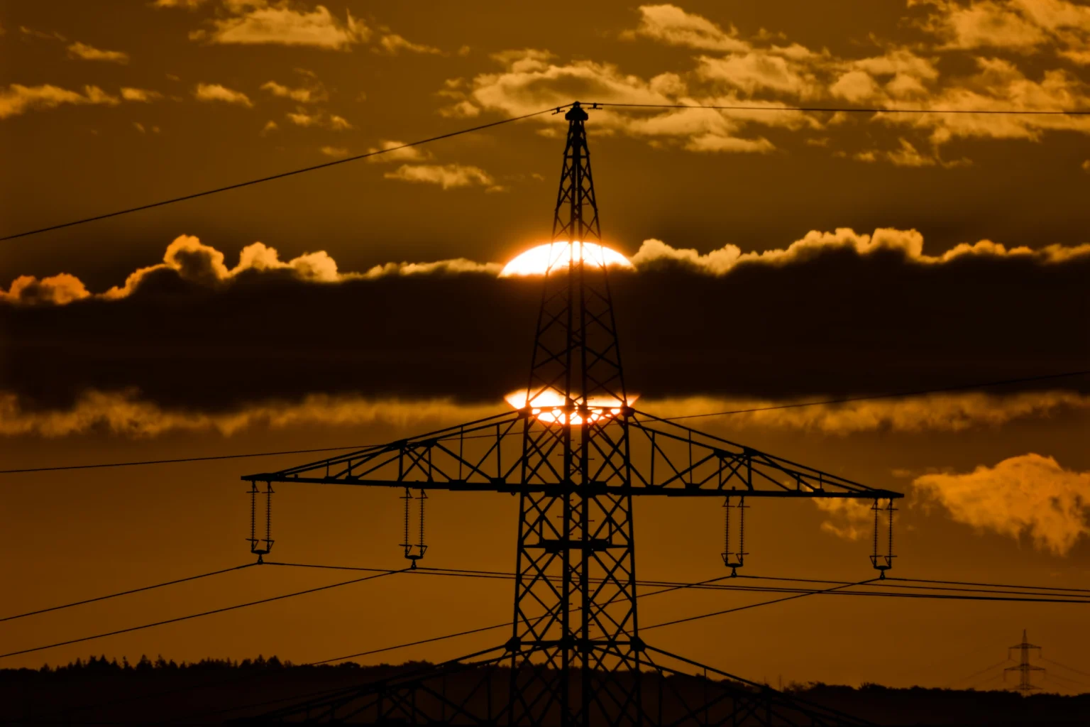 Sonnenaufgang hinter Wolken und einem Strommast.